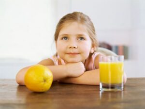 girl sitting at a table with an orange and a glass of juice